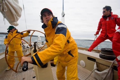 A maritime specialist in yellow storm gear controls a sailing yacht at sea